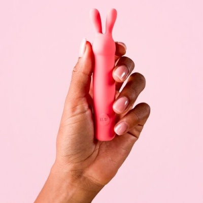 Mão a segurar vibrador pequeno cor-de-rosa em fundo rosa