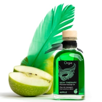Óleo de massagem verde em garrafa de vidro ao lado de maçã verde cortada e pena verde