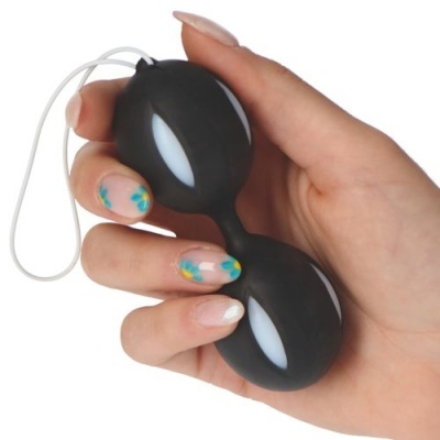 Dispositivo preto em forma de ovos duplos com detalhes brancos, segurado por mão com unhas pintadas com flores azuis e amarelas