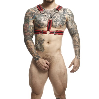 Homem com arnês de peito preto e vermelho, com tatuagens visíveis em fundo branco.