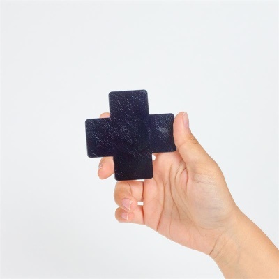 Peça preta em forma de cruz segurada por mão com fundo branco