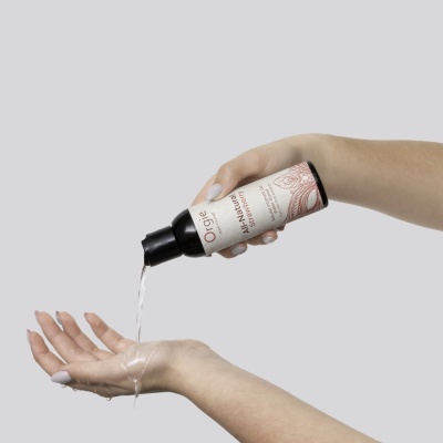 Mãos despejam líquido de um frasco preto com rótulo branco e design floral