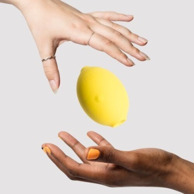 Mãos segurando objeto amarelo em forma de limão sobre fundo cinza