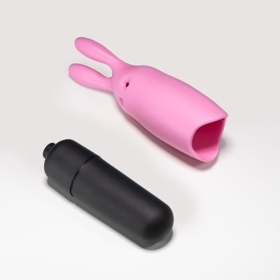 Objeto rosa em forma de coelho com orelhas e objeto preto cilíndrico em fundo branco