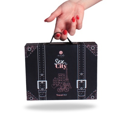 Estojo preto Sex in the City Travel Kit com ilustrações e texto, segurado por mão com unhas vermelhas