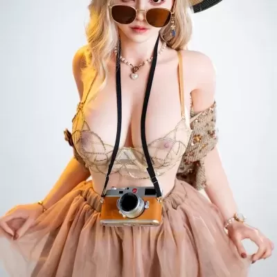 Mulher com chapéu de palha, óculos de sol, colar, sutiã dourado, saia godê e câmara fotográfica à volta do pescoço.