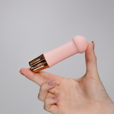 Dispositivo cor-de-rosa com base dourada segurado por mão com unhas nude