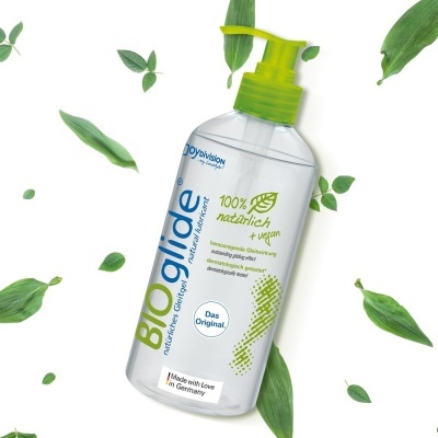 Frasco de lubrificante BIOglide com doseador verde e folhas verdes ao redor