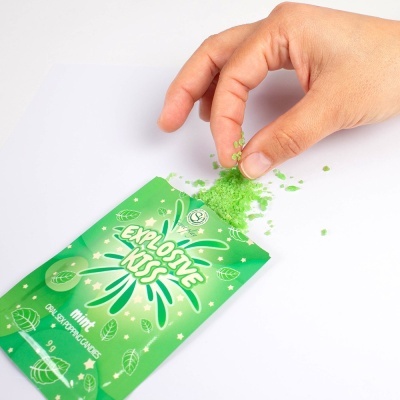Pacote verde de balas efervescentes de hortelã e mão a pegar balas.