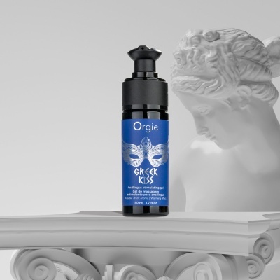 Frasco azul e preto de gel Orgie Greek Kiss sobre coluna jónica branca com escultura clássica ao fundo
