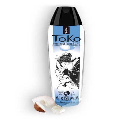 Frasco de lubrificante Toko com rótulo azul e branco e tampa preta junto a pedaços de coco