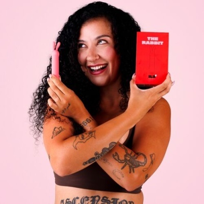 Mulher sorridente segura vibrador rosa e embalagem vermelha THE RABBIT