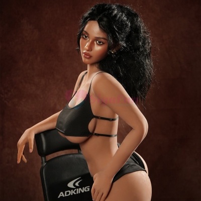 Boneca realista com roupa preta junto a cadeira ADKING em fundo castanho