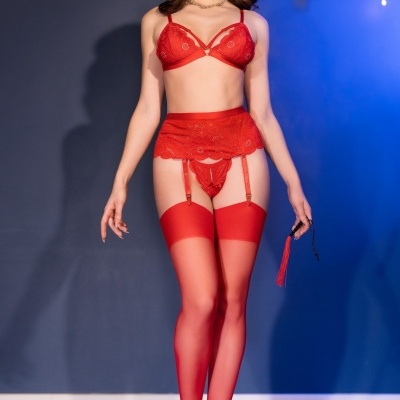 Modelo feminina veste lingerie vermelha em renda com sutiã, cinta-liga, calcinha e meias transparentes, em fundo azul.