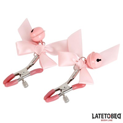 Par de prendedores metálicos rosa com laços e campainhas sobre fundo branco