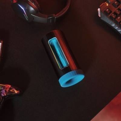 Dispositivo cilíndrico preto e azul com texto njoy sobre mesa preta, auscultadores e teclado ao fundo.