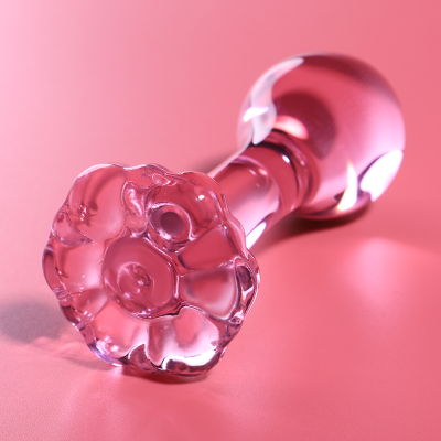 Frasco de vidro rosa translúcido com tampa decorativa em flor numa superfície rosa.