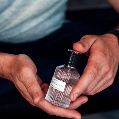Frasco de perfume transparente com rótulo SCENTED nas mãos de um homem