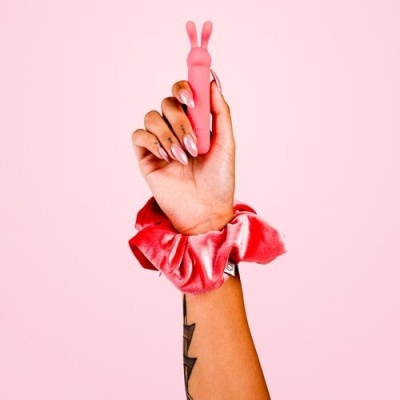Mão segurando objeto rosa em forma de coelho com fita de cabelo rosa no pulso