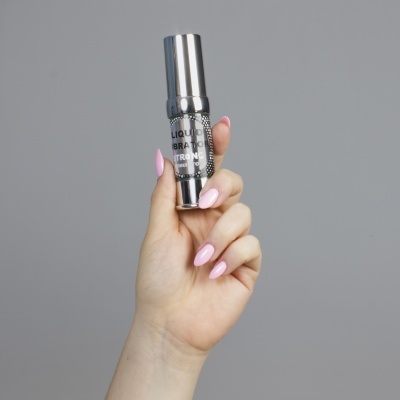 Mão feminina segura frasco metálico prateado com texto LIQUID VIBRATOR STRONG STIMULATOR