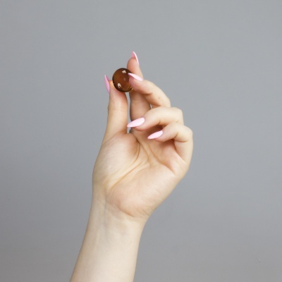 Mão com unhas rosa a segurar cápsula castanha