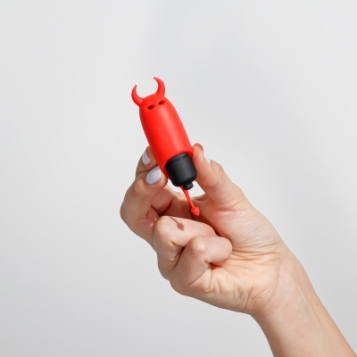 Objeto vermelho com pontas curvas segurado por mãos com unhas brancas num fundo branco.