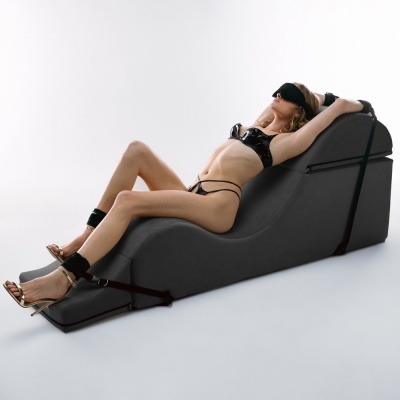 Mulher de lingerie preta e máscara reclinada em cama ergonómica preta com cintas pretas