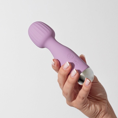 Massageador manual lilás com textura estriada e botões, segurado por mão com unhas feitas