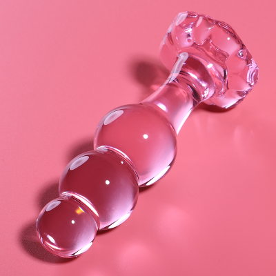 Objeto de vidro transparente com três esferas em sequência e base decorativa sobre superfície rosa