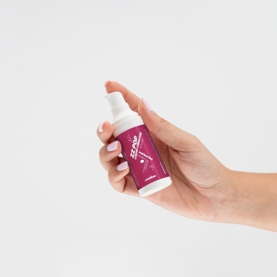 Mão segurando frasco branco com rótulo roxo e tampa de bomba.