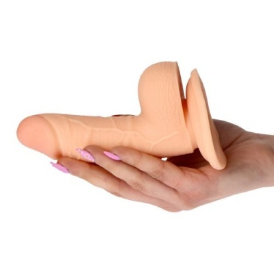 Dildo cor de pele com ventosa na base segurado por mão com unhas rosa