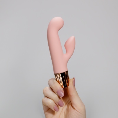 Vibrador cor-de-rosa com base dourada segurado por mão com unhas rosas