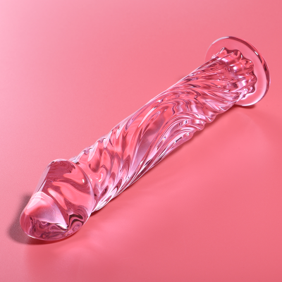 Dildo transparente com textura ondulada e base larga sobre superfície cor-de-rosa