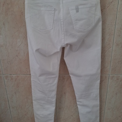 Calças denim brancas penduradas numa parede de azulejos com etiquetas visíveis no cós e bolso