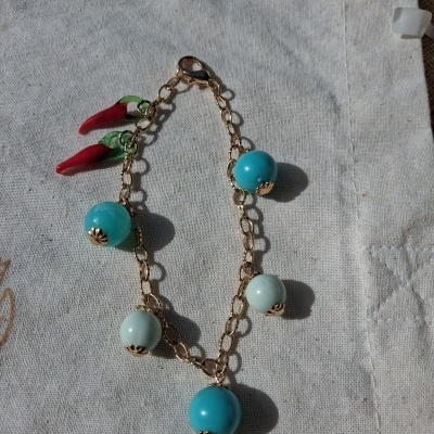 Pulseira dourada com bolas azuis, verdes e pimentas vermelhas em tecido claro