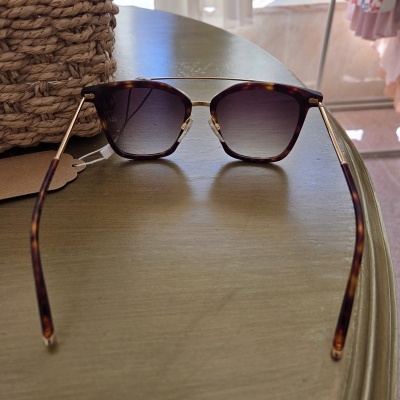 Óculos de sol de padrão tartaruga castanha com lentes escuras e armação dourada sobre mesa de madeira.