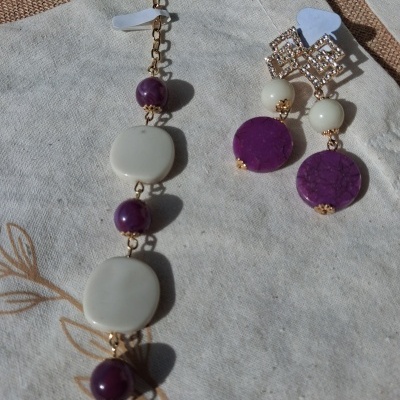 Colar e brincos roxo e branco com corrente dourada sobre tecido cru