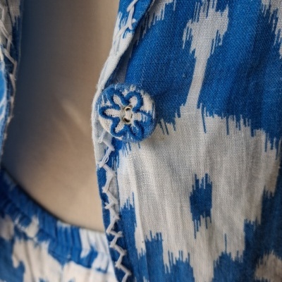Peça de roupa azul e branca com padrão Ikat, botão forrado bordado e costura decorativa