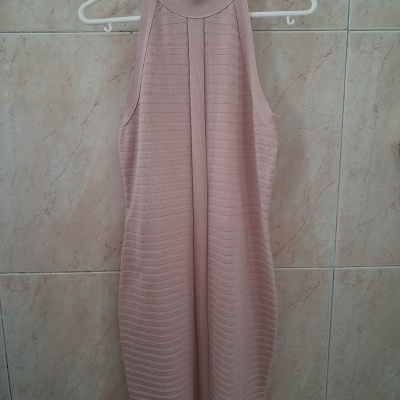 Vestido cor-de-rosa com padrão de nervuras pendurado num cabide branco em parede de azulejos creme