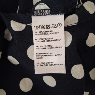 Etiqueta de roupa em tecido preto com bolinhas brancas mostrando instruções de lavagem e composição polyester