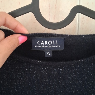 Etiqueta de roupa preta com texto branco CAROLL Collection Cachemire XS e mão segurando em cabide preto