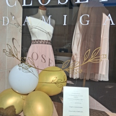 Vitrine de loja com vestidos pasteis em manequins e balões dourados e brancos