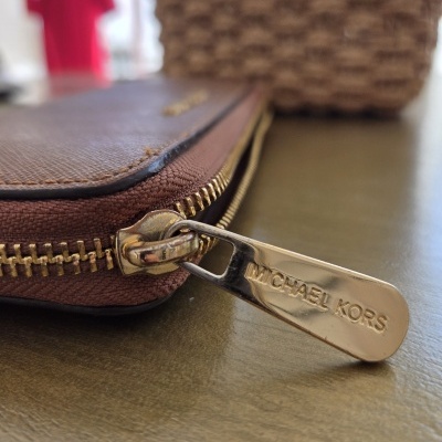 Puxador dourado de carteira castanha com texto MICHAEL KORS em foco.