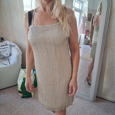 Vestido bege claro com textura metálica e alças pretas em mulher junto a espelho