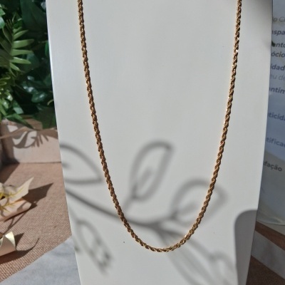 Colar dourado com corrente entrelaçada no suporte branco