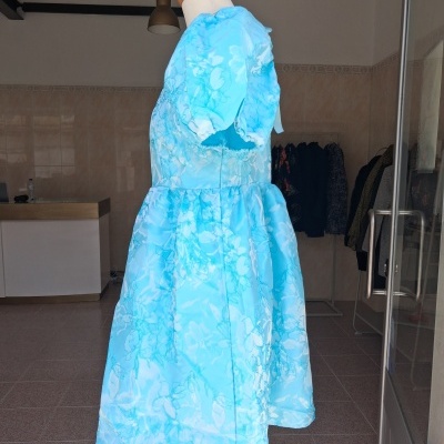 Vestido infantil azul claro com padrão floral branco numa loja.