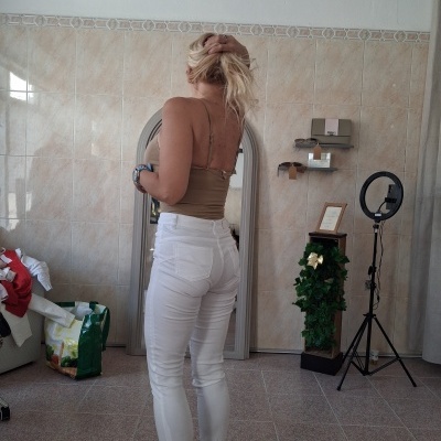 Mulher de costas com calças brancas e top castanho em interior com azulejos e espelho
