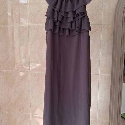 Vestido castanho-escuro com folhos e gola elástica pendurado num cabide cinzento.