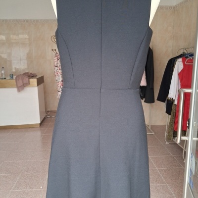 Vestido cinza escuro sem mangas visto de costas em manequim dentro de loja de roupa.