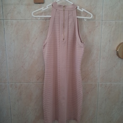 Vestido rosa claro pendurado em cabide branco contra azulejos bege